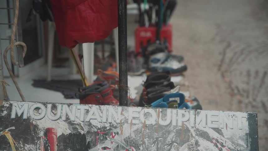 Boots lined up on a stoop behind a sign advertising mountain equipment