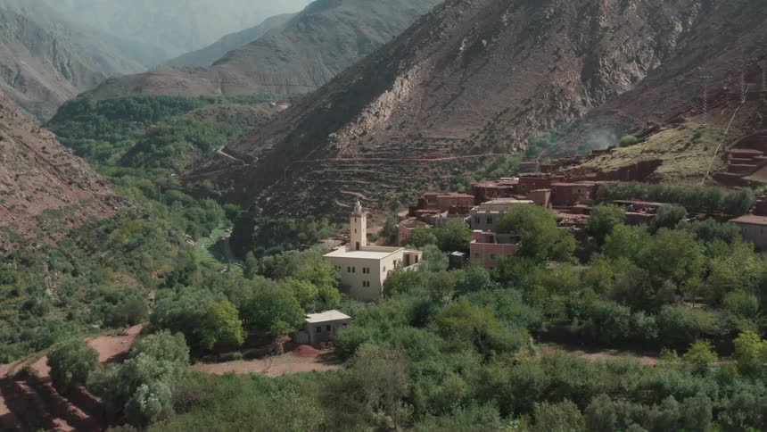A verdant mountain valley with a mosque and its minaret standing out among earthtoned village buildings