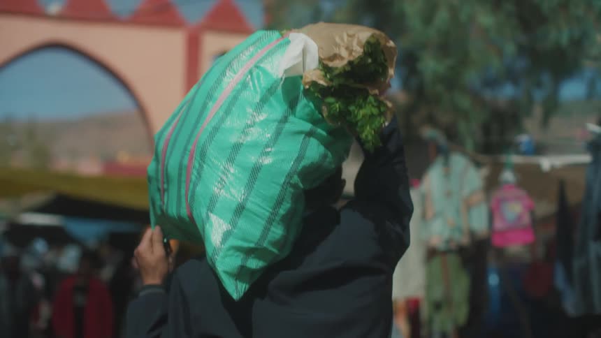 Man carries a bag of groceries in an open farmer street market