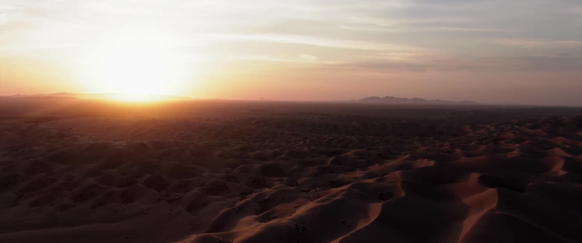 A desert region with sand dunes and a very bright sun in the sky