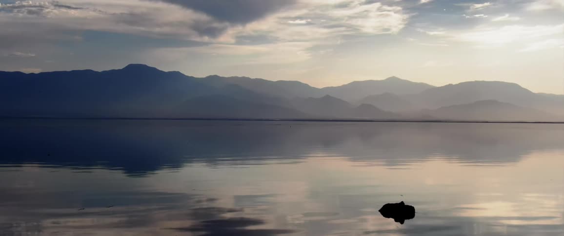 A landscape of a region with water reflecting the sky and behind huge mountains