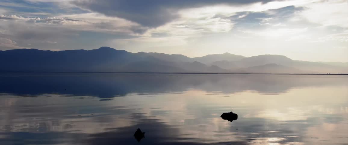Landscape of a calm sea with a mountain range on the horizon under a morning sky