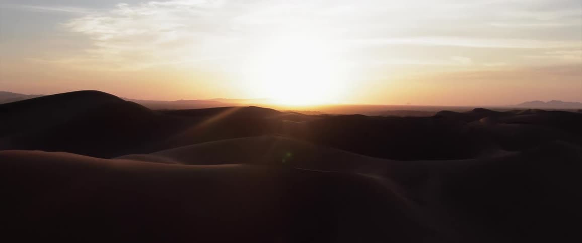 Rising sun shines across desert terrain on a cloudy day