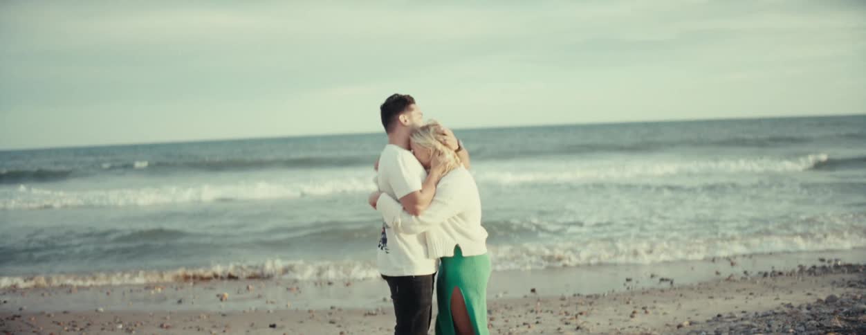 Man and woman stand on beach on windy day hugging