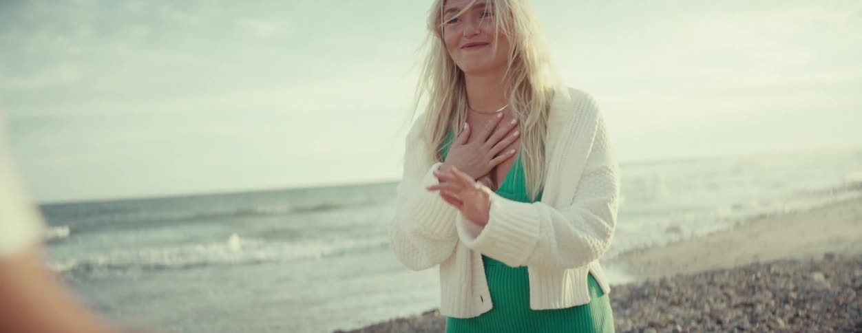 Man walks to woman laughing on beach and takes her hand