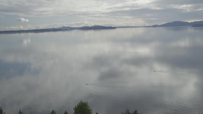 Revealing two sea kayakers moving through calm water with islands in the distance