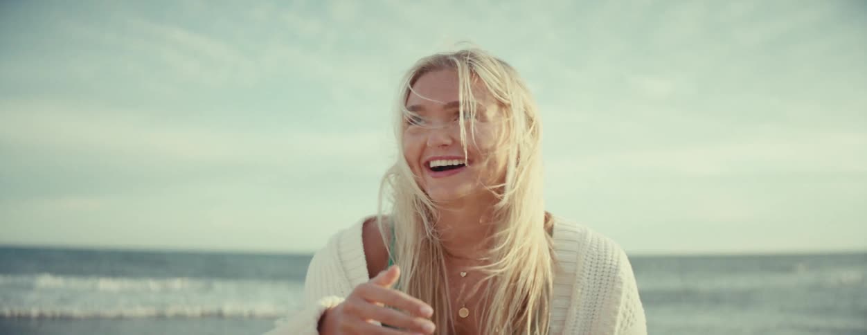 Portrait of a woman on the beach taking her hand off her mouth and extremely happy