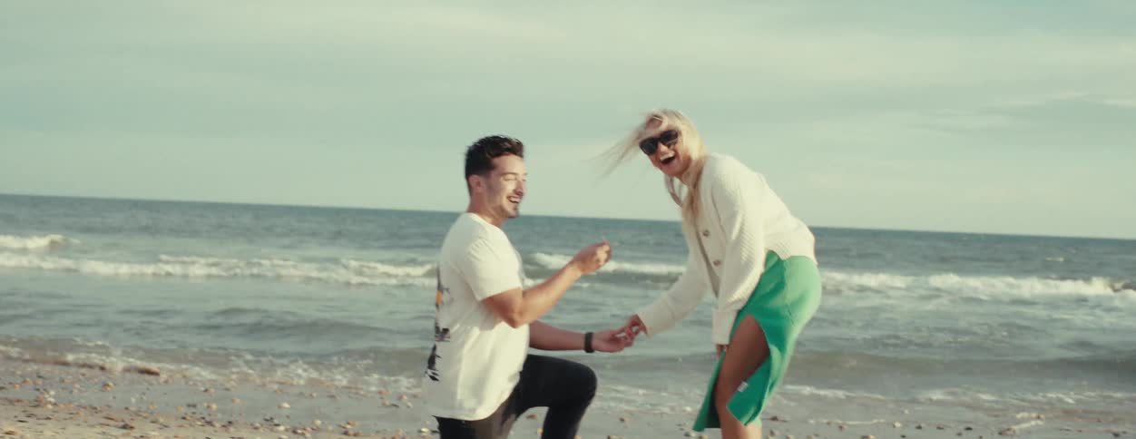 A man kneeling on the beach as he propose to a woman with a ring on a sunny day