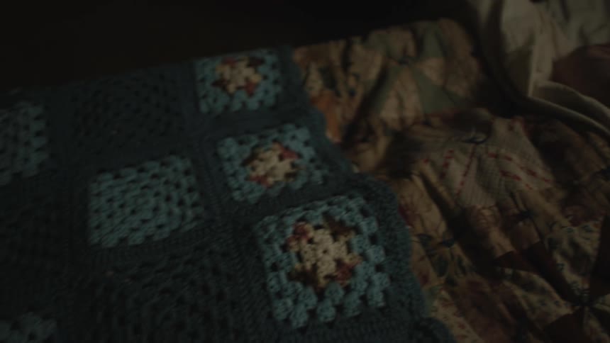 Elderly female invalid lies on bed under an afghan