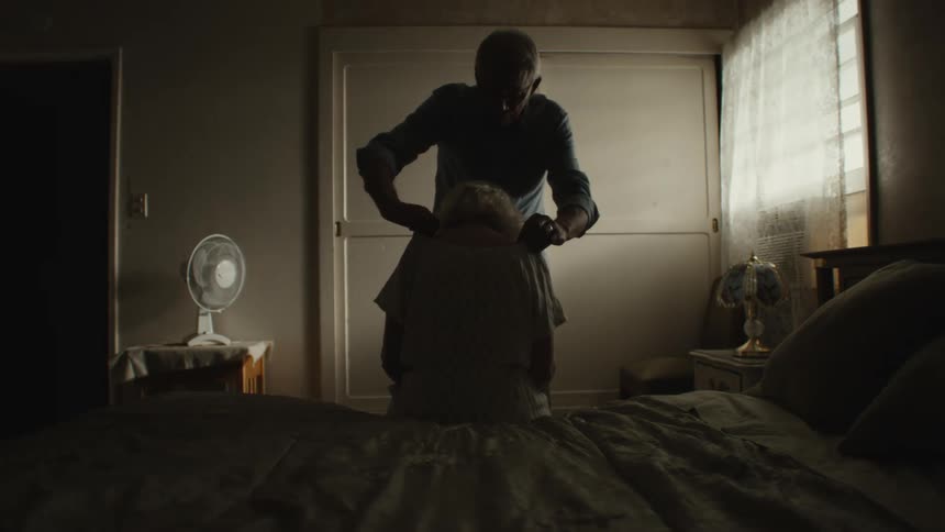 An elderly man helping his wife get dressed
