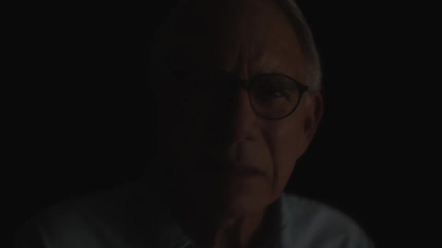 An elderly man wearing glasses looking sad as times goes between night and day fast