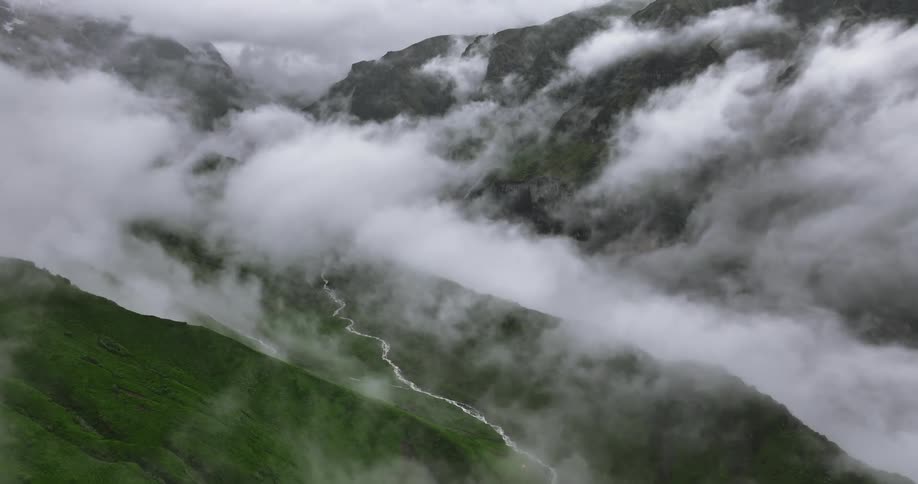 An aerial view of a valley between mountains covered in vegetation and lots of clouds overhead