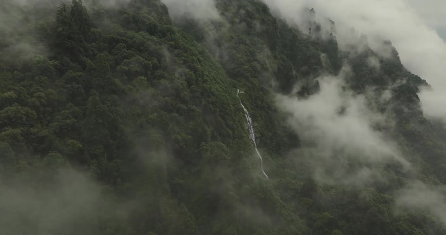A small waterfall in a mountain of trees and many misty clouds in the sky