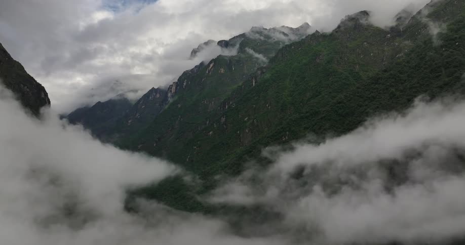 A mountainous region with mountains covered in vegetation and several clouds nearby
