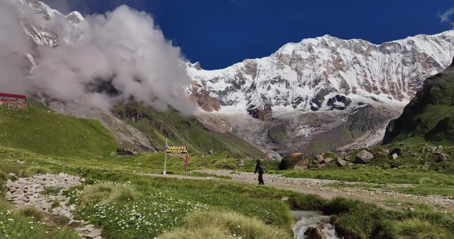 Person walking on a natural road in a landscape with snowcovered mountains under a blue sky