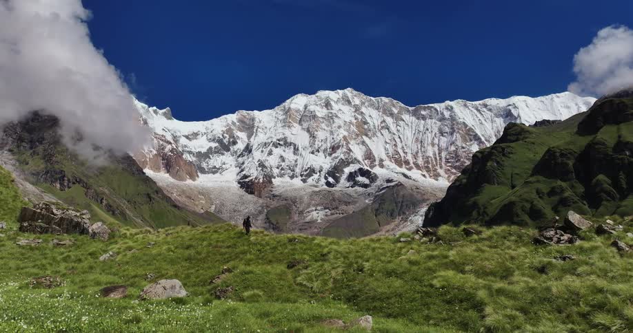 A person passing by a grassy hill and behind snowy mountains