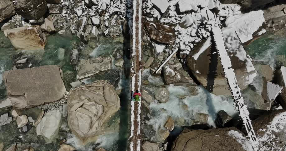 A persong hiking and crossing a bridge as water flows by under the bridge during winter