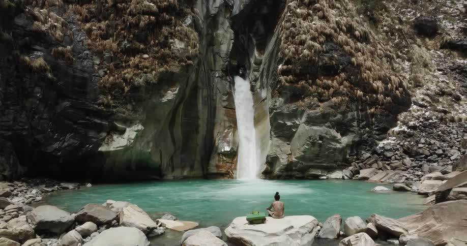 Woman sitting on a rock facing a natural waterfall in turquoise waters
