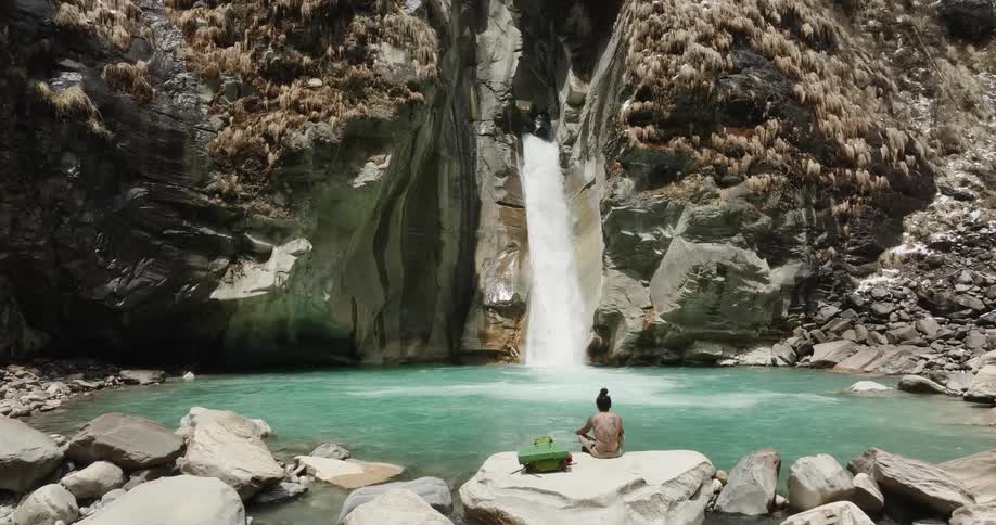 A person meditating in a waterfall with blue water