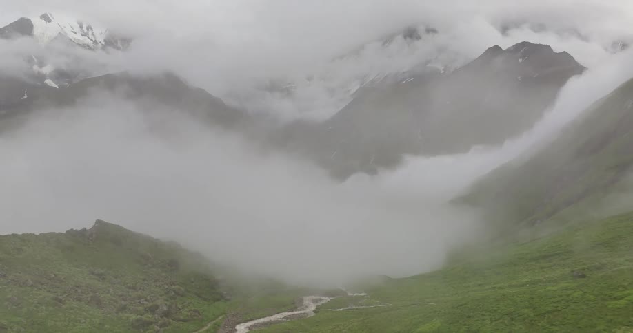 Landscape of a riverbed and snowcovered mountains at cloud level