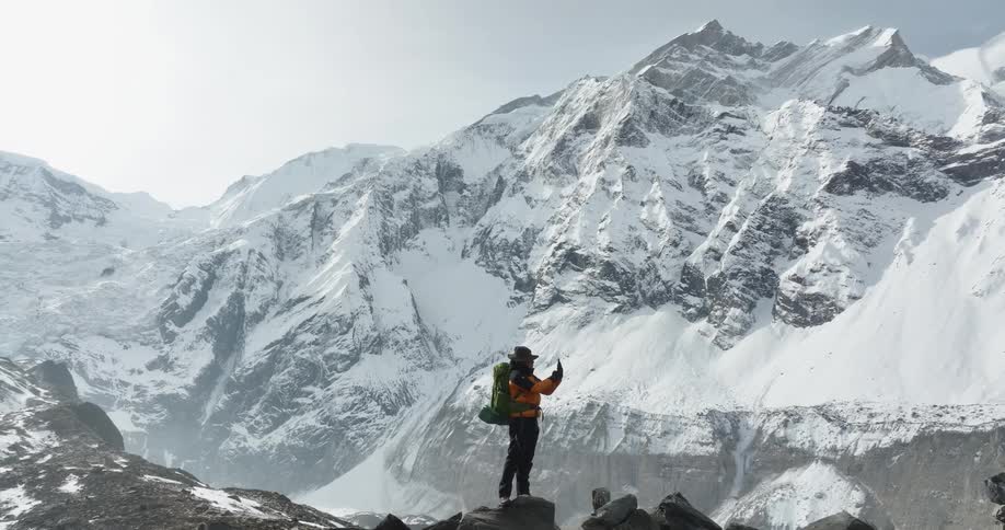 A hiker on a ridge taking a photo of a snowy mountain range with a smart phone