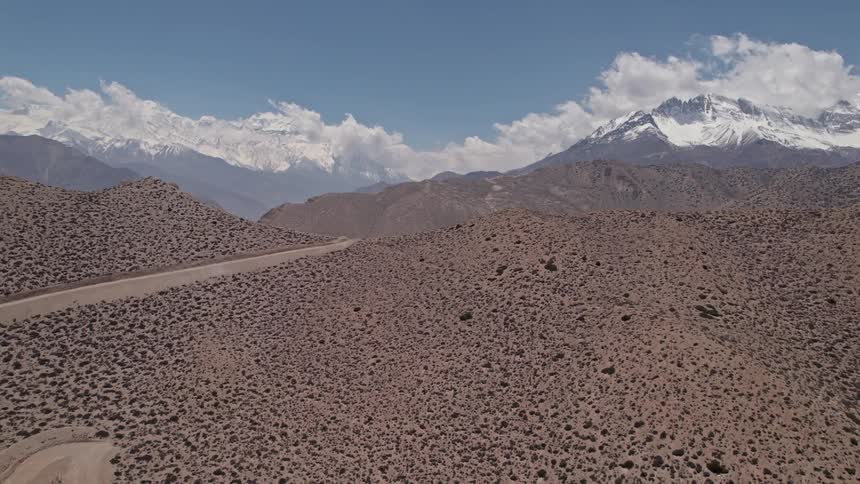 Aerial panorama of arid mountains and other mountain ranges in the background covered in snow