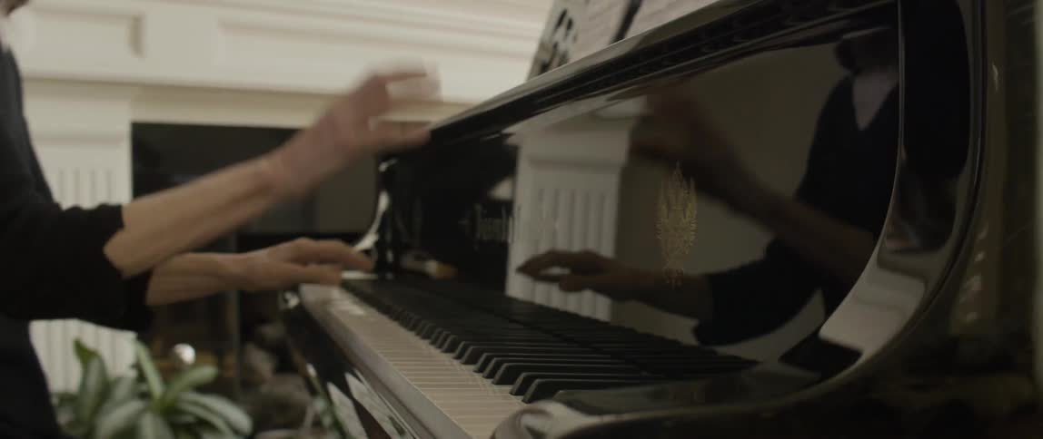 A woman playing the piano by a fireplace in a sunny room