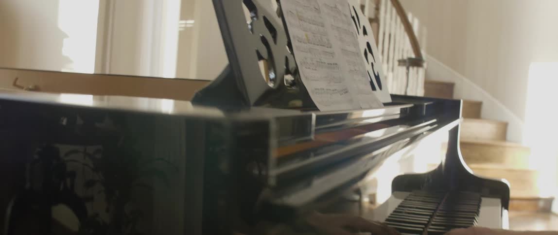 A woman playing a piano by a winding staircase