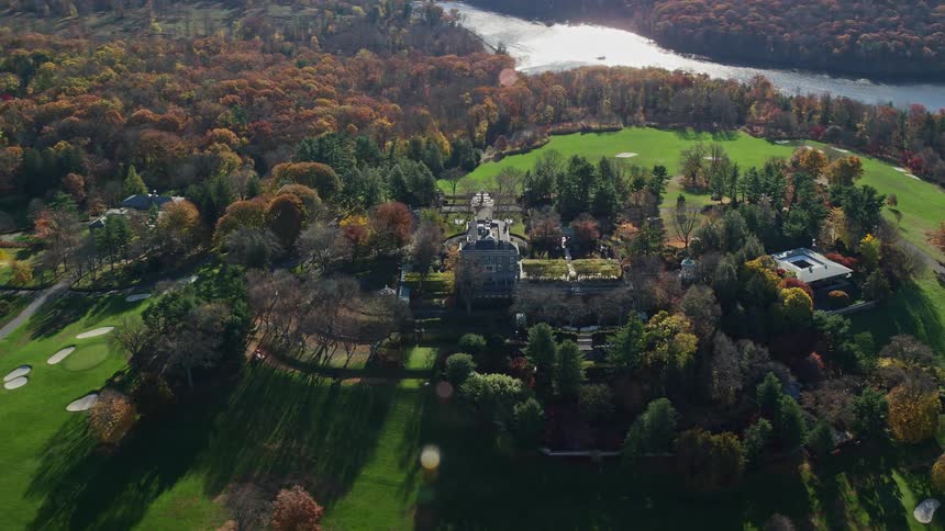Aerial of buildings and golf course encircled by woods and water during the fall