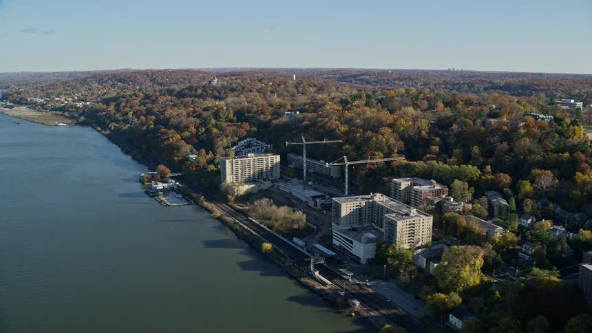 Aerial of construction cranes at sites near water in heavily wooded area during the fall
