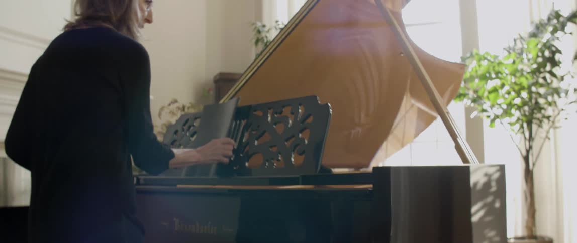A woman closes a book of sheet music on a piano and walks away