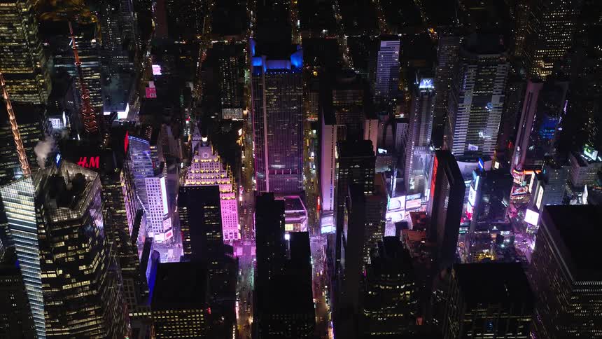 A street in a city with huge buildings is being illuminated by many bright lights