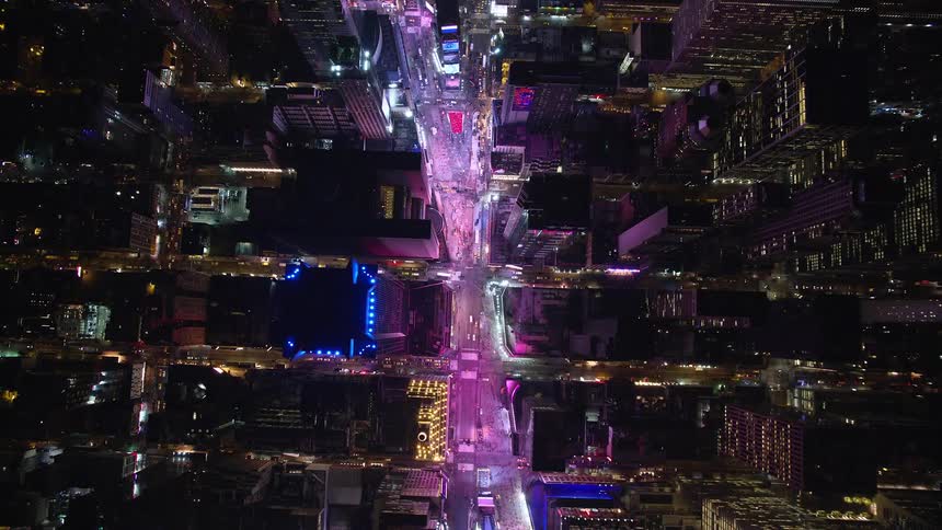 Aerial of large brightly lit major downtown street paralleling and intersecting dimly lit streets