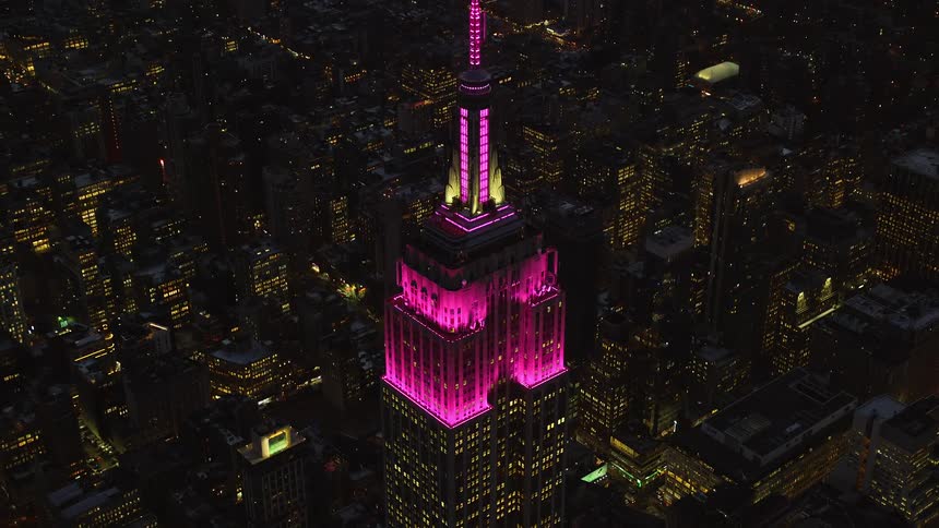A skyscraper building in the middle of the city is shining pink light at the top in the night
