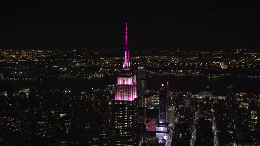 Aerial view of a metropolis at night with prominent pinklit skyscrapers by the seaside
