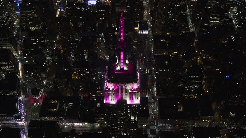 Aerial of pink light topped skyscraper towering over cityscape at night