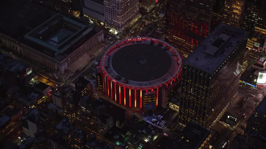 Aerial panorama of a circular building illuminated in red at night in the midst of a metropolis