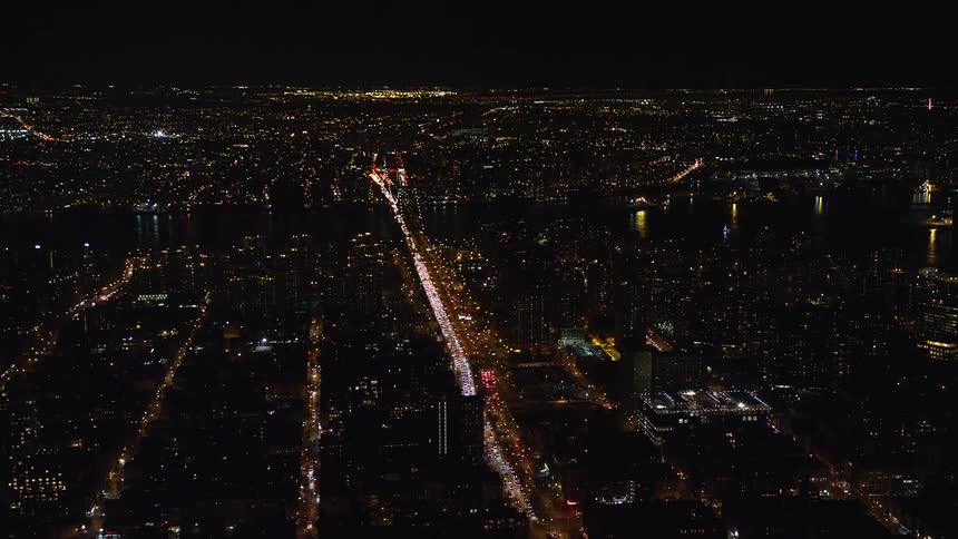 Aerial view of a nighttime metropolis by the seaside with a central highway and traffic