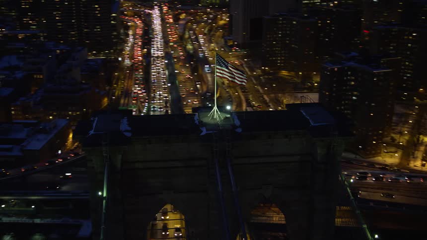 Bridge in the midst of a nighttime metropolitan city with a usa flag on top