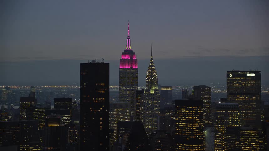 A metropolitan city at night with building lights on and a building has pink light on top