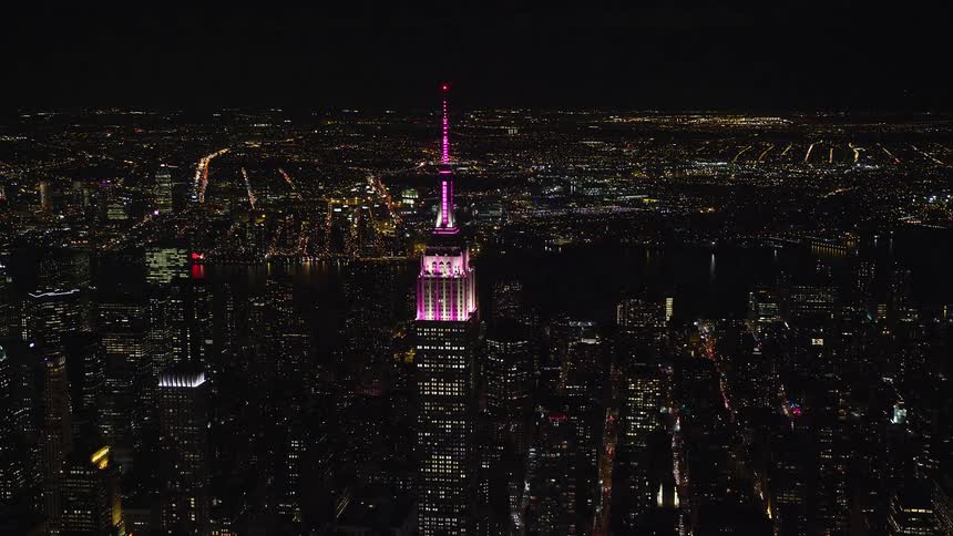 Aerial view of a central tower with pink lights in the midst of a nighttime metropolis