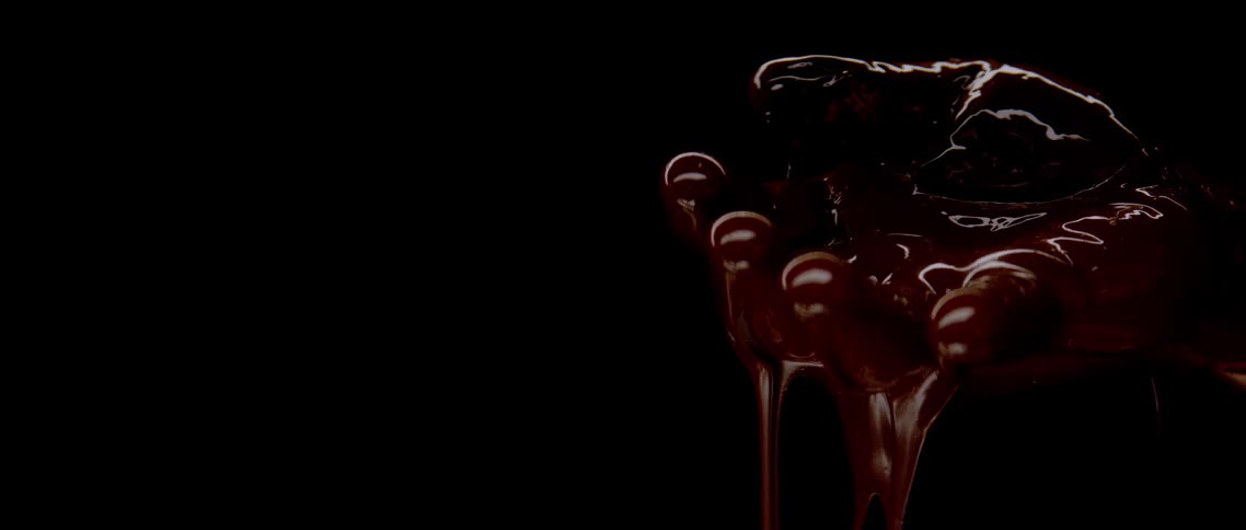 A chocolate dripping down from a round surface in a dark room