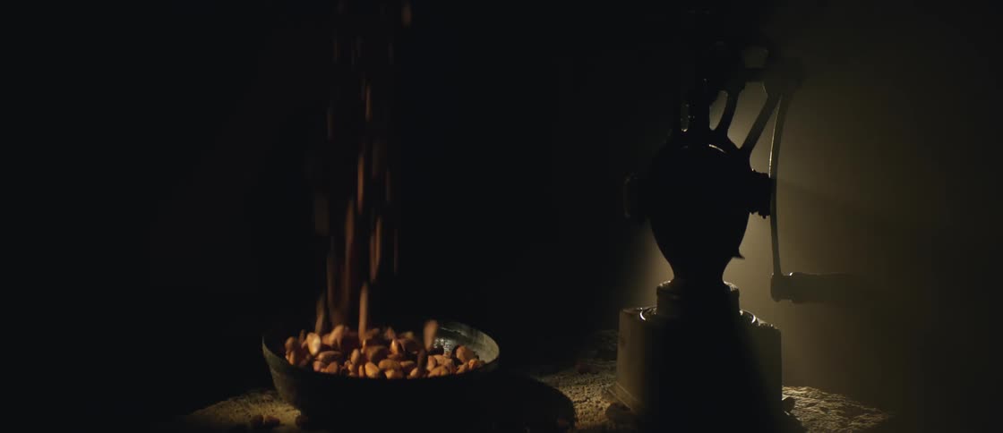 Coffee beans fall on a plate near a vintage grinder