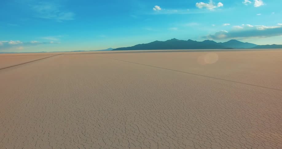 Aerial view of a dry and desert terrain with a mountain range on the horizon under a blue sky