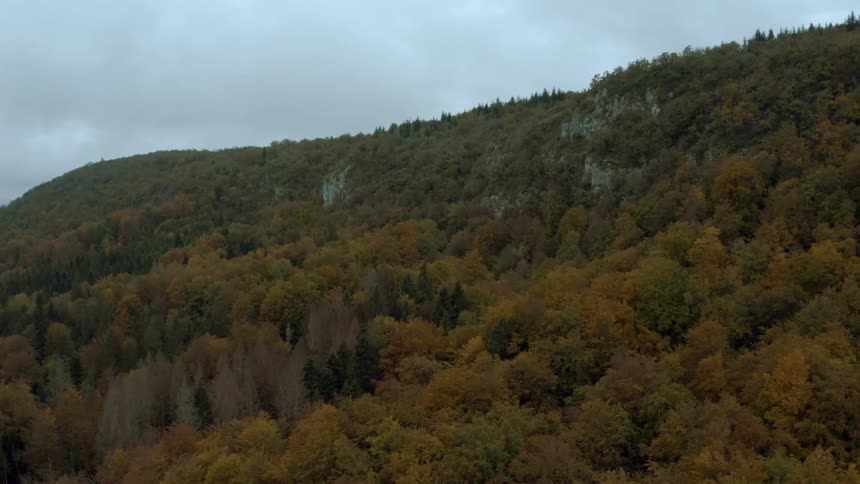 Forested mountain with trees in fall colors under a cloudy sky