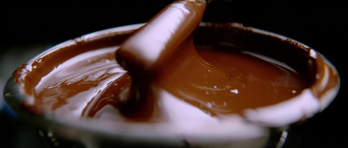 Spatula slowly rising in a stream of melted chocolate