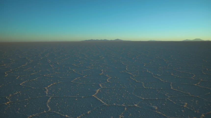Cracked ground across the desert with mountains in the distance under a blue hazy sky