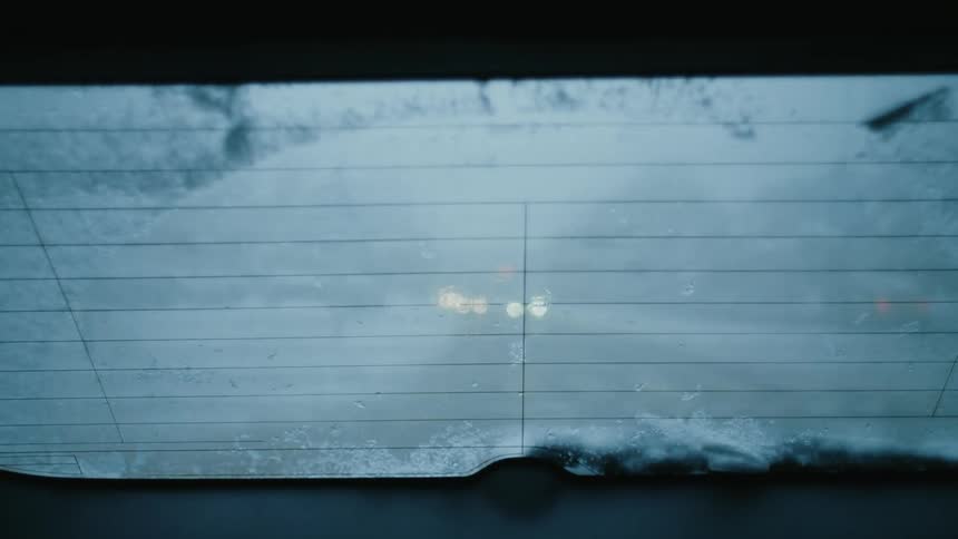 Headlights of other vehicles are visible through partially ice covered rear window