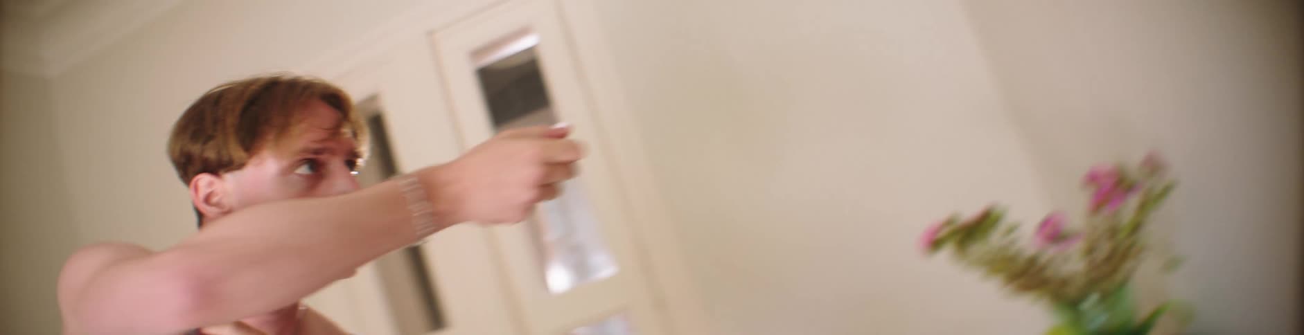 Man with light blue undershirt dances beside a wall
