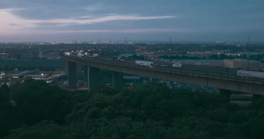 Aerial view of a highway bridge with vehicles on it and a city at the horizon at dawn